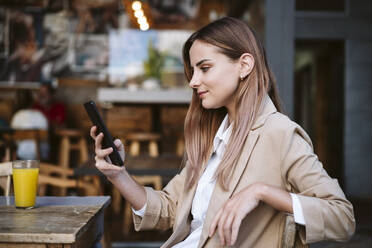 Young businesswoman using smart phone at cafe terrace - EBBF04718