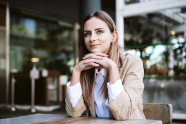 Young businesswoman with hands clasped sitting at cafe terrace - EBBF04721