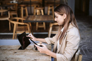 Female business professional using digital tablet at cafe table - EBBF04723