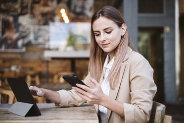 Geschäftsfrau mit digitalem Tablet und Smartphone auf der Terrasse eines Cafés - EBBF04727