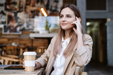 Thoughtful businesswoman with disposable cup at coffee shop terrace - EBBF04731