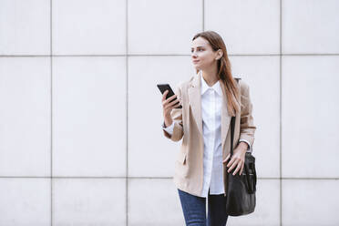 Female business professional with shoulder bag standing in front of wall - EBBF04738