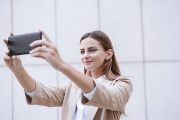 Geschäftsfrau nimmt Selfie durch Handy vor der Wand - EBBF04749