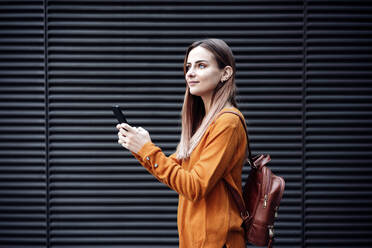 Woman with backpack and mobile phone by wall - EBBF04774