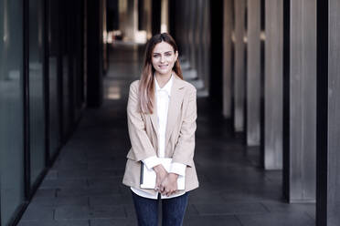 Businesswoman holding digital tablet while standing at corridor - EBBF04783