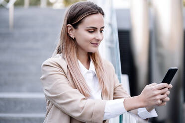 Businesswoman using smart phone while standing at railing - EBBF04791