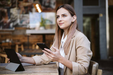 Geschäftsfrau mit Mobiltelefon und digitalem Tablet in einem Café sitzend - EBBF04795
