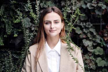 Young female professional with blond hair standing by plants - EBBF04799