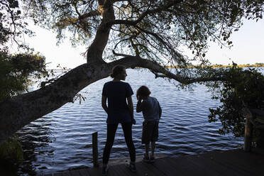 Two children on the edge of a waterway, rear view, Okavango Delta - MINF16460