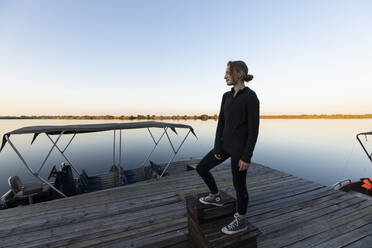 Teenage girl, silhouette at dusk, on a jetty on the Okavango Delta - MINF16464