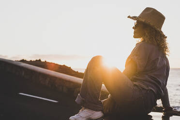 Mature woman wearing hat while sitting on car during sunset - SIPF02557