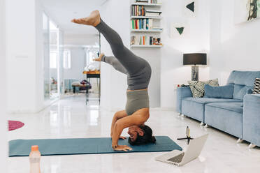 Female vlogger doing headstand while filming home workout tutorial in living room - JRVF01883