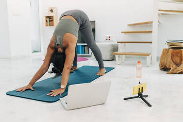 Weibliche Influencerin macht Yoga, während sie ein Workout-Tutorial im Wohnzimmer filmt - JRVF01885