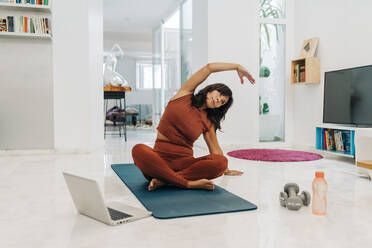 Aktive Frau, die Yoga übt, während sie zu Hause mit dem Laptop lernt - JRVF01895