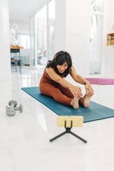 Weibliche Influencerin macht Yoga, während sie zu Hause über ihr Handy vloggt - JRVF01897
