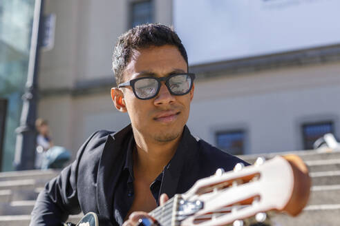 Gut aussehender männlicher Gitarrist mit Brille, der an einem sonnigen Tag Gitarre spielt - IFRF01065