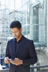 Junger Geschäftsmann, der mit seinem Smartphone vor einem Bürogebäude Textnachrichten verschickt - IFRF01068
