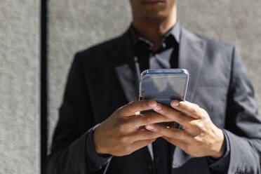 Male professional using smart phone in front of wall during sunny day - IFRF01083