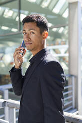 Gutaussehender Mann, der vor einem Bürogebäude steht und mit seinem Handy telefoniert - IFRF01094