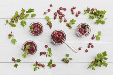 Raw gooseberries (Ribes uva-crispa) and jars of homemade gooseberry jam lying on white table - GWF07183