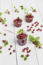 Raw gooseberries (Ribes uva-crispa) and jars of homemade gooseberry jam lying on white table - GWF07185