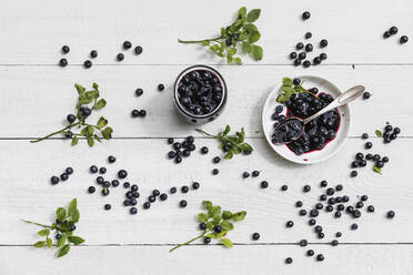 Rohe Heidelbeeren und ein Glas hausgemachte Heidelbeermarmelade auf einem weißen Tisch - GWF07187