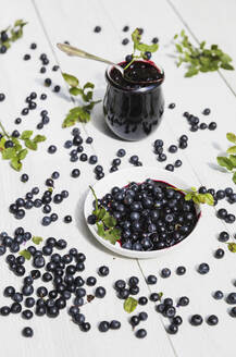 Rohe Heidelbeeren und ein Glas hausgemachte Heidelbeermarmelade auf einem weißen Tisch - GWF07188