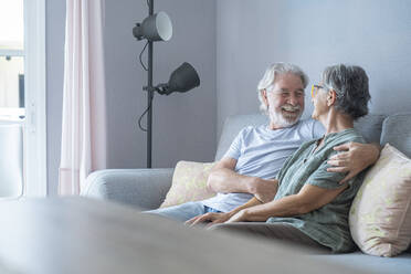 Lächelnder älterer Mann mit Hand auf der Schulter, der eine Frau im Wohnzimmer ansieht - SIPF02561