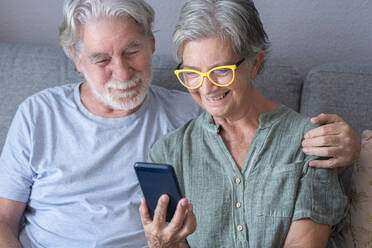 Smiling senior woman sharing smart phone with man at home - SIPF02567
