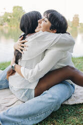 Smiling lesbian women hugging while sitting on grass - JRVF01915