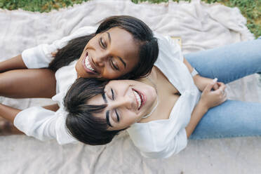 Happy lesbian couple sitting back to back on blanket - JRVF01918