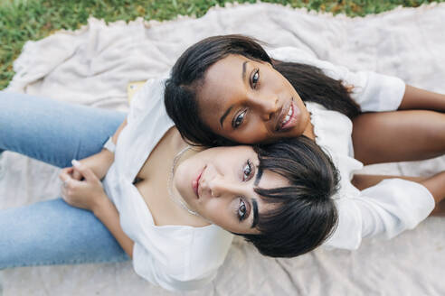 Lesbisches Paar sitzt Rücken an Rücken auf einer Decke - JRVF01919