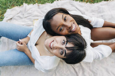 Smiling girlfriends sitting on blanket - JRVF01920