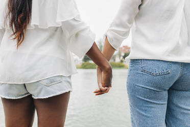 Girlfriends holding hands at lakeshore - JRVF01944