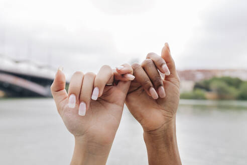 Lesbian couple holding fingers by lake - JRVF01956