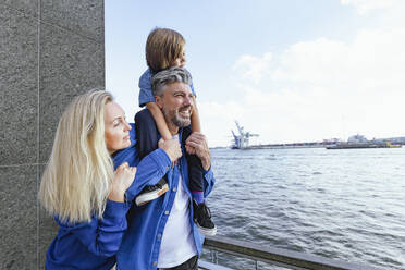 Lächelnde Familie mit Blick auf den Fluss, während sie an der Reling steht - IHF00563