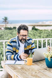 Bärtiger Mann mit Laptop und Mobiltelefon am Tisch - SIPF02585