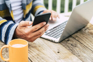 Mann mit Laptop und Smartphone bei der Arbeit am Tisch - SIPF02593