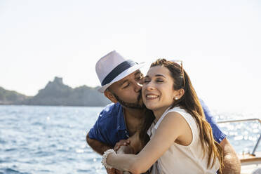 Man kissing woman while leaning on motorboat railing - EIF02104