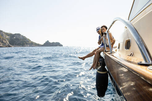 Mid adult couple sitting at the edge of motorboat during sunny day - EIF02105