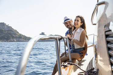 Smiling couple sitting at motorboat edge during sunny day - EIF02107