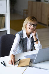 Mid adult businesswoman sitting at desk in office - GIOF13713