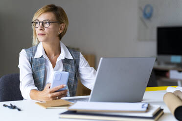 Businesswoman with mobile phone sitting at desk in office - GIOF13715