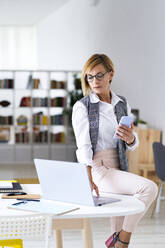 Mid adult female professional using laptop while sitting on desk in office - GIOF13731