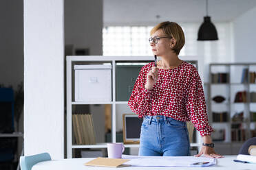 Thoughtful female professional standing at desk in office - GIOF13745