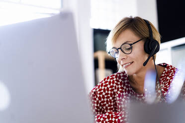 Female customer service representative wearing headphones while working in office - GIOF13760