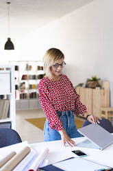 Lächelnde Geschäftsfrau öffnet Laptop am Schreibtisch - GIOF13761