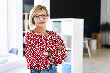 Confident businesswoman standing with arms crossed in office - GIOF13772