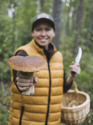 Lächelnde Frau zeigt Steinpilz im Wald - KNTF06441
