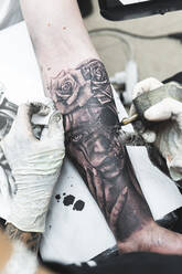 Künstlerin beim Tätowieren auf dem Arm eines männlichen Kunden im Studio - JAQF00847